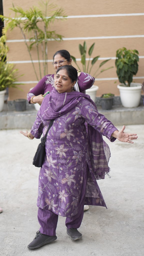 A guest in a purple salwar kameez, arms open in welcome