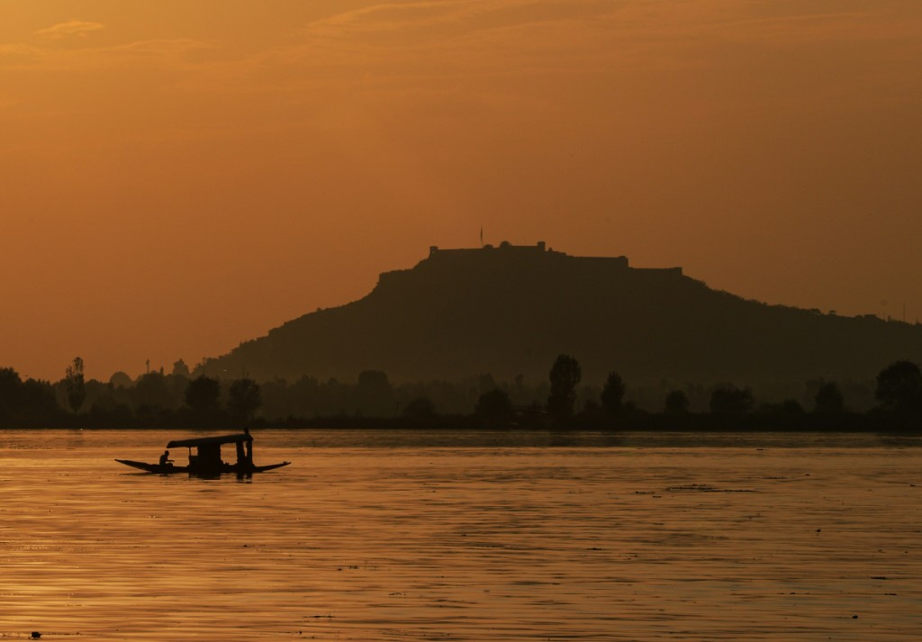 Shikara gliding across Dal Lake at sunset with houseboats in the background